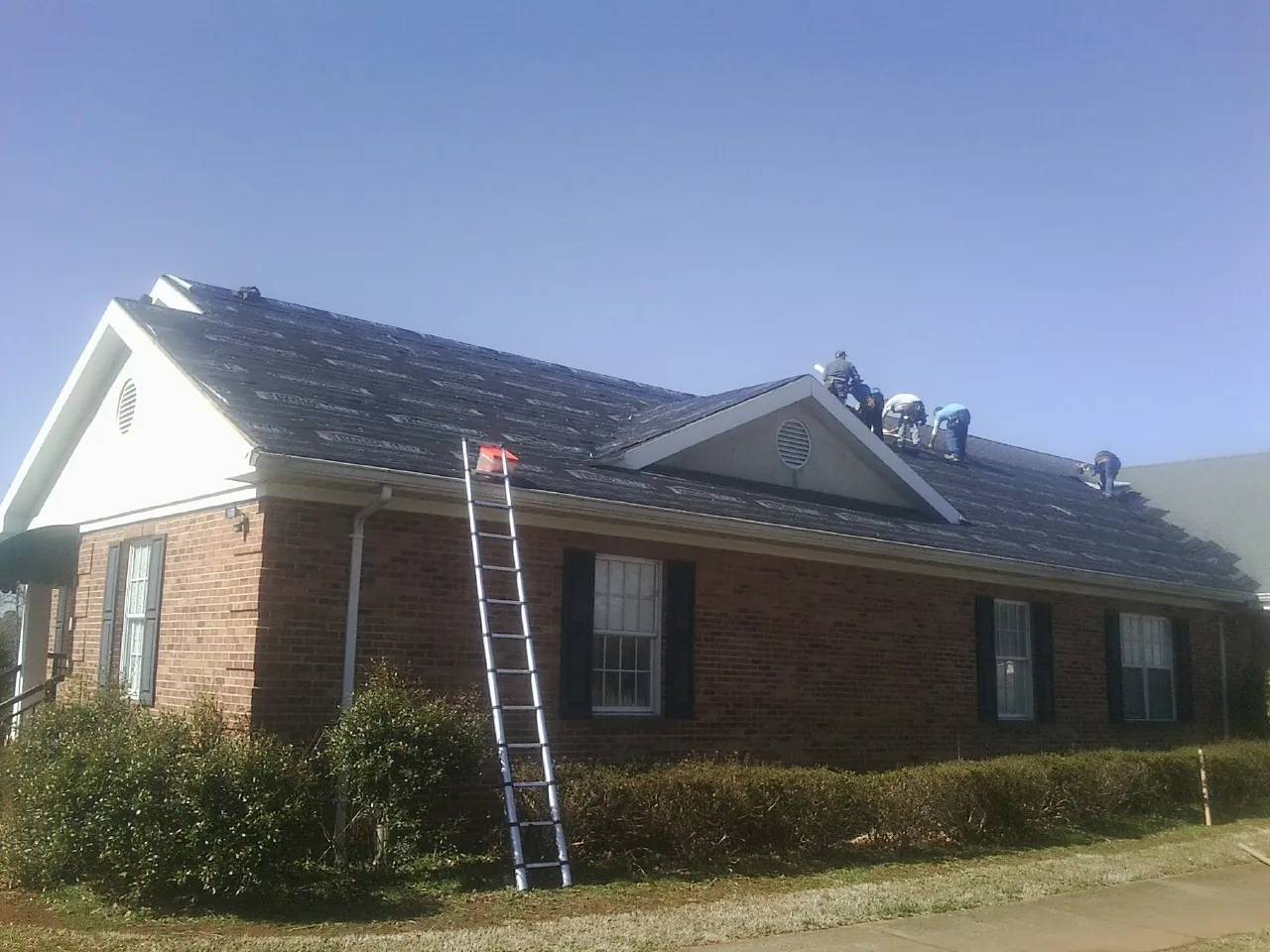 Crew tearing shingles off a brick ranch roof with a ladder set — Metal Roof Repair work by our crew in La Salle